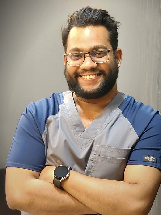 Dr. Ali Rashid in clinic scrubs, smiling with his arms crossed